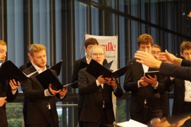 Junge Männer singen und blicken auf die Hände eines Dirigenten
