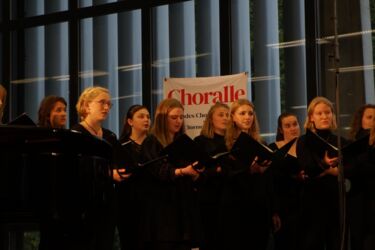Junge Sängerinnen im Chor vor einem Schild mit der AUfschrift Choralle